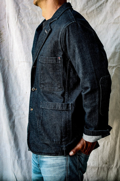 Side view of indigo denim chore blazer showing patch pockets, elbow patch and cuffed selvedge sleeve.