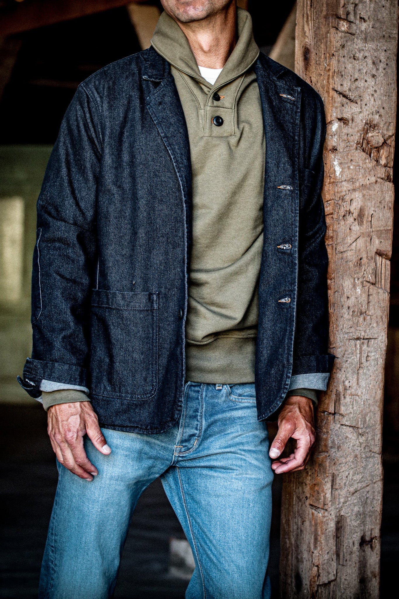 Man wearing a dark indigo denim chore blazer open over an olive shawl-collar henley and faded jeans.