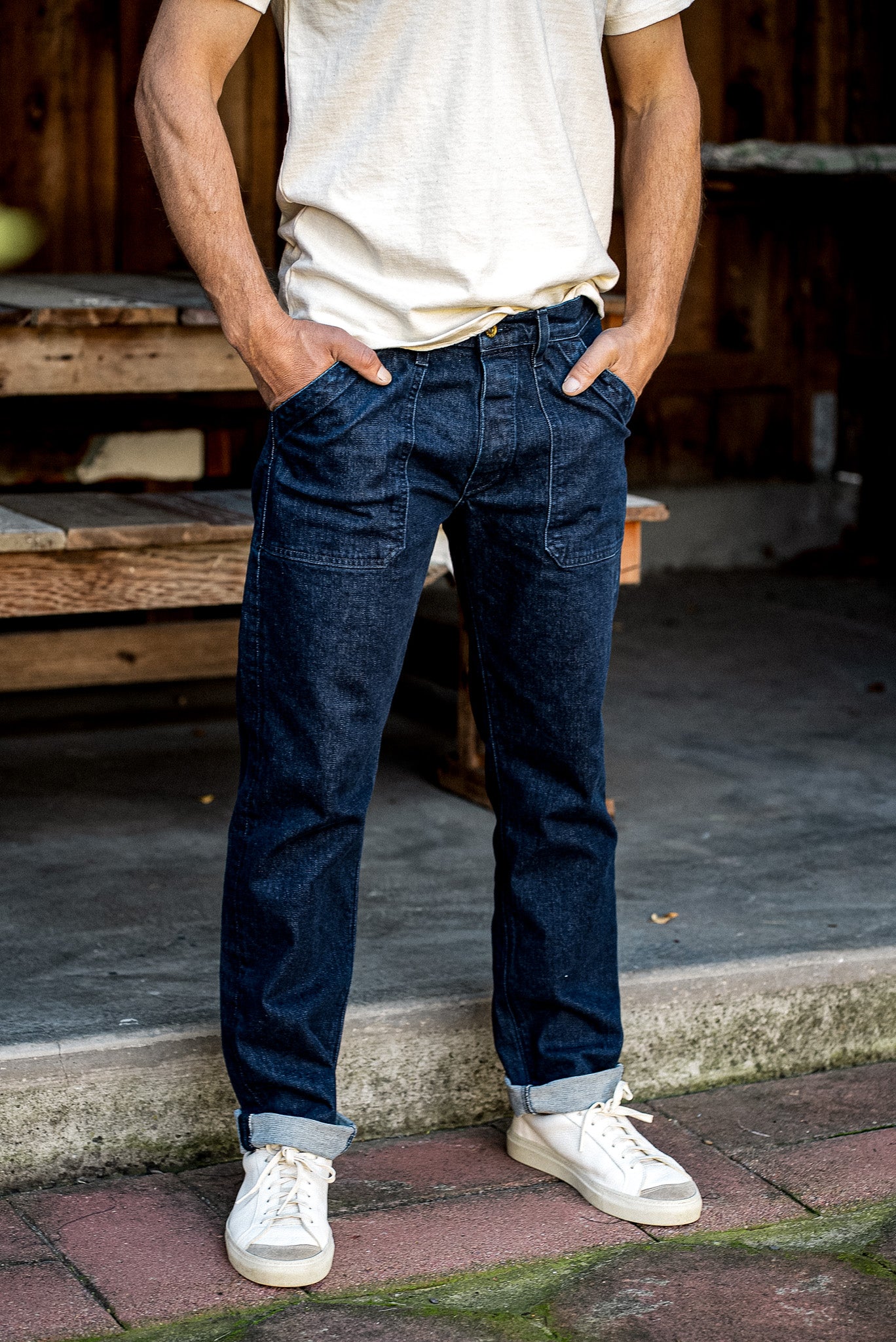 Scout military jean in dark Ocean wash denim, worn cuffed with cream sneakers.