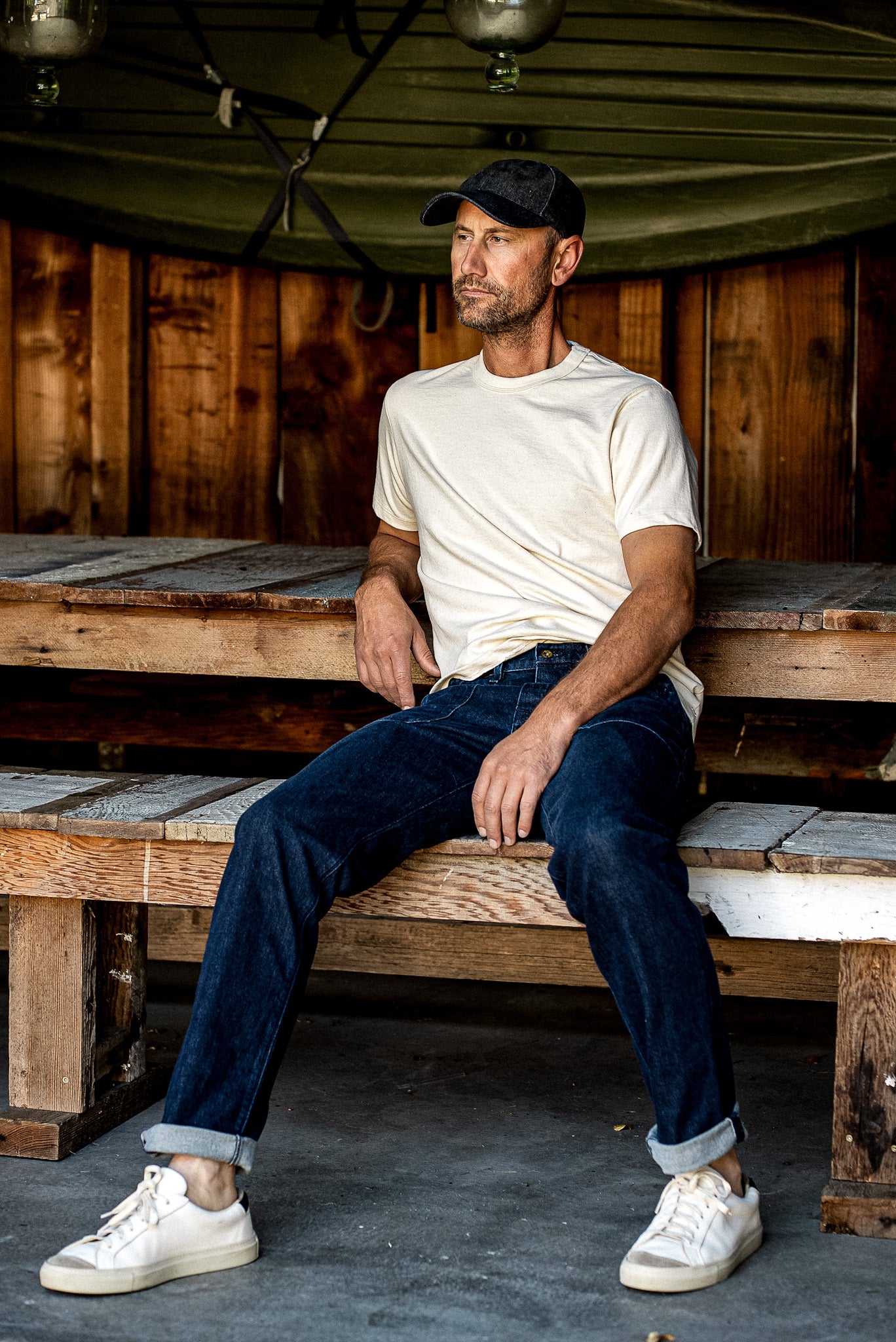 Ocean wash Scout denim military pant with cuffed hems, worn seated on a wooden bench.