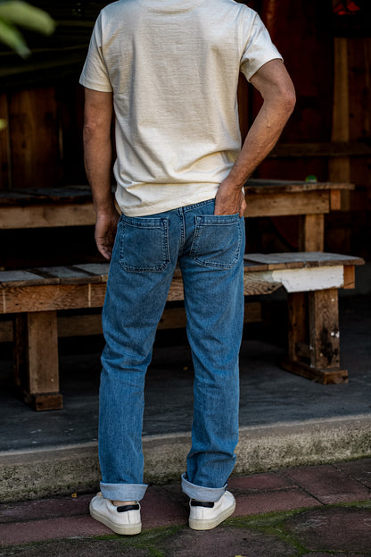 Rear view of salt-wash selvedge denim jeans with patch back pockets and cuffed hems, worn with a cream tee.