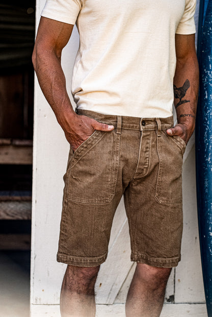 Model in wheat-colored denim military shorts with slanted front pockets, paired with a cream tee.