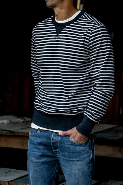 Man wearing a navy and cream striped Stinson rugby jersey pullover with blue denim jeans.