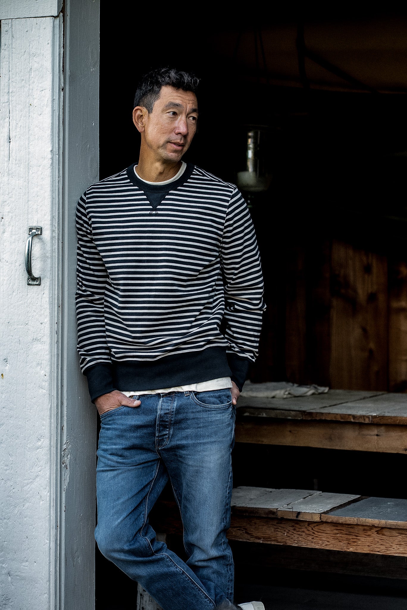 Man in navy and cream striped Stinson rugby jersey pullover and jeans leaning in a doorway.