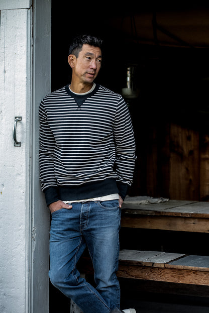 Man in navy and cream striped Stinson rugby jersey pullover and jeans leaning in a doorway.