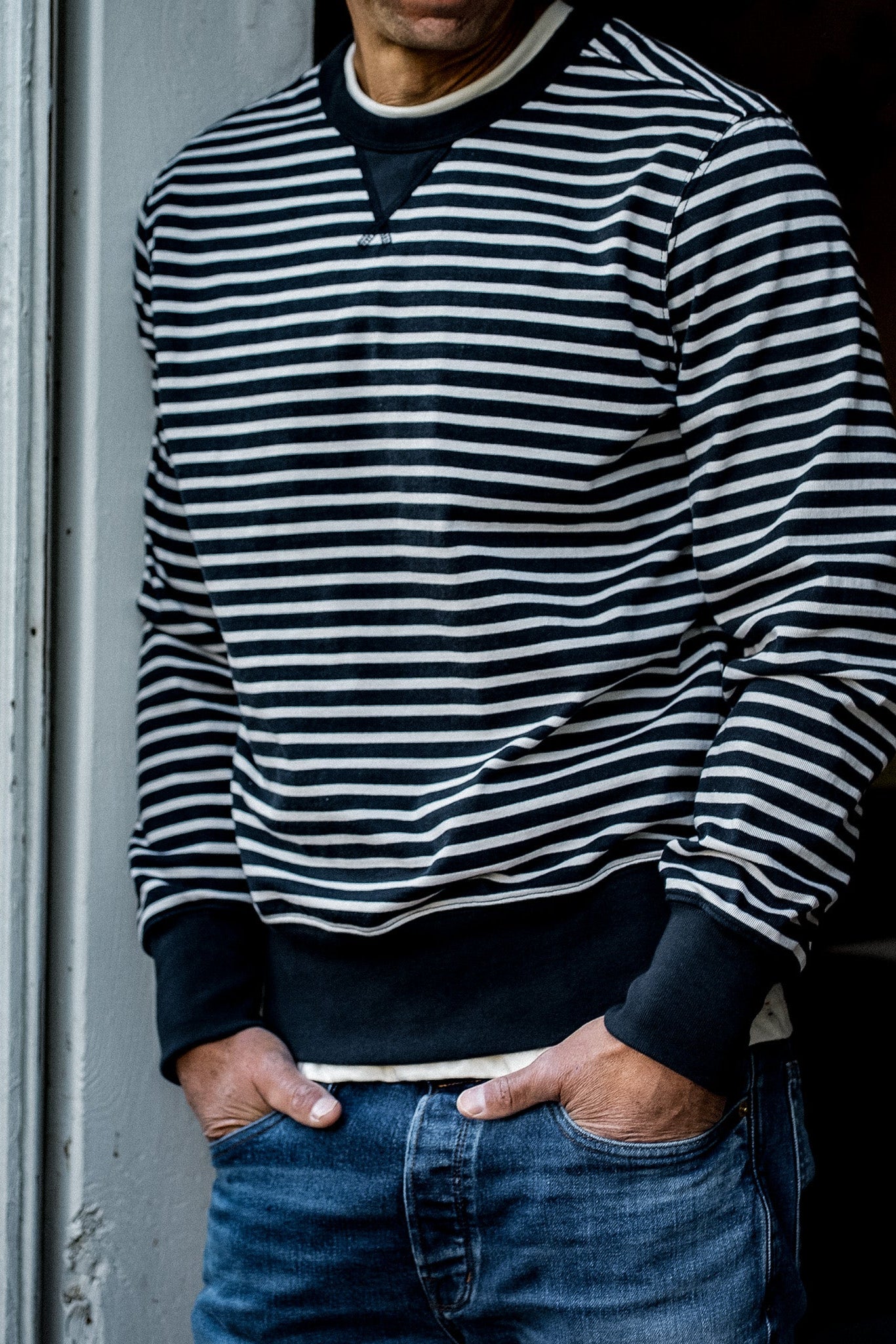 Man in navy and cream striped rugby jersey pullover with hands in denim jeans pockets.