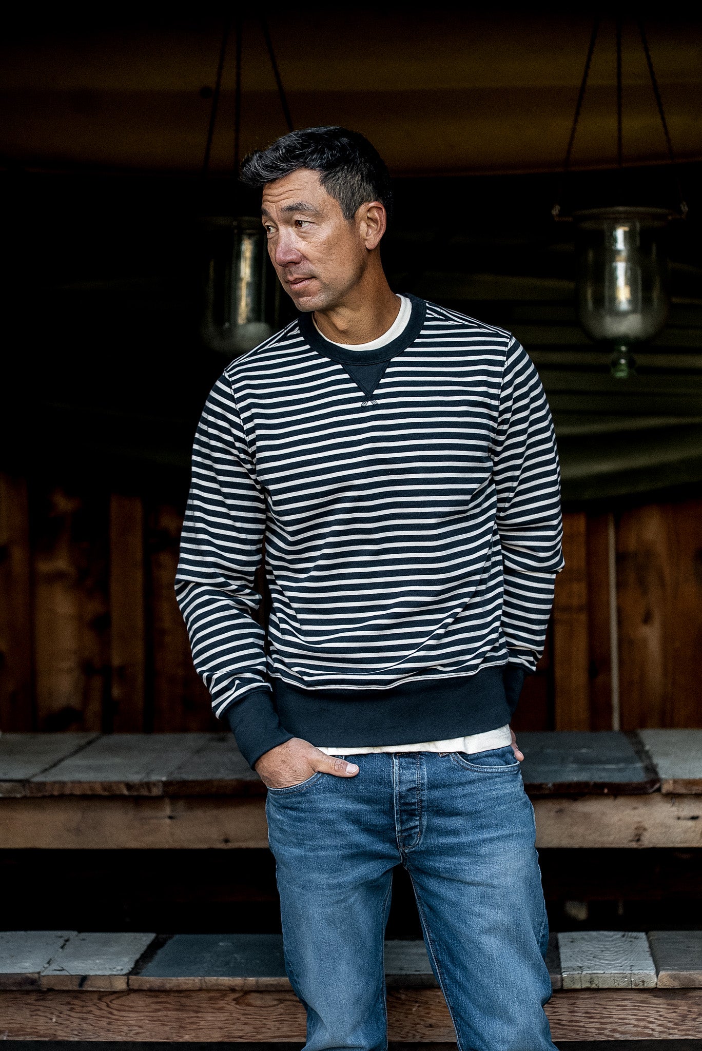 Man in a navy and cream striped Stinson rugby jersey pullover and blue jeans on a wooden porch.