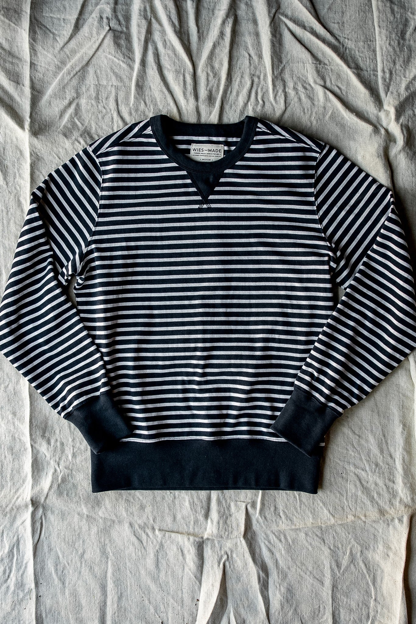 Navy and white striped rugby jersey pullover with black ribbed cuffs and hem, laid flat on canvas.