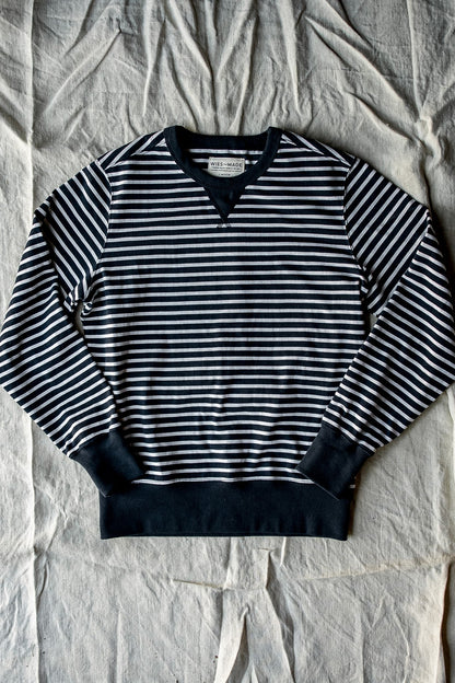 Navy and white striped rugby jersey pullover with black ribbed cuffs and hem, laid flat on canvas.