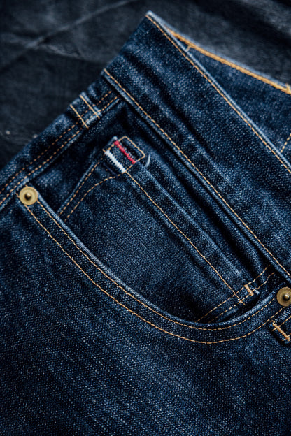 Real denim jeans with a close-up view of the pocket, featuring contrast stitching, brass rivets, and selvedge detailing.