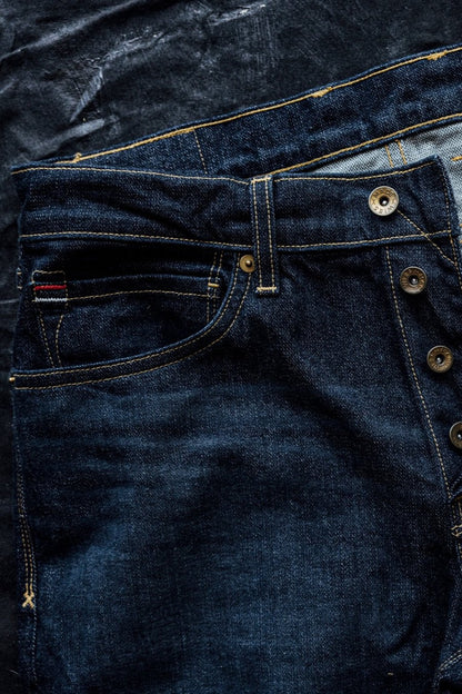 Dark American denim jeans with contrast stitching, button fly, and selvedge detailing, laid flat on a textured black background.