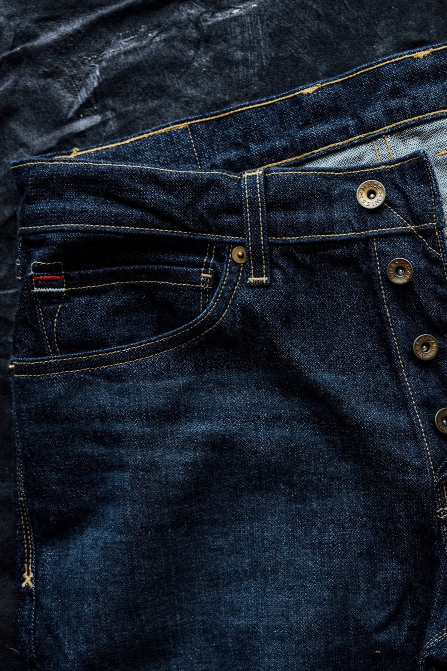 Close-up of ocean wash American-made denim jeans showing brass button fly, contrast stitching, and pocket detail.