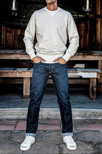 Man in a cream sweatshirt and ocean wash straight slim American made jeans with cuffed hems and white sneakers.