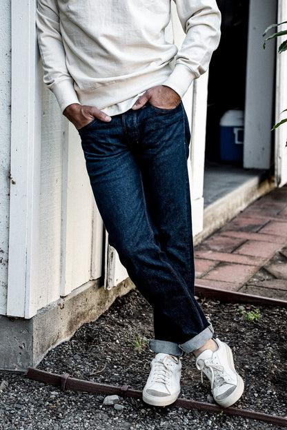 Man in cream sweatshirt and white sneakers wearing cuffed ocean wash American made denim jeans.