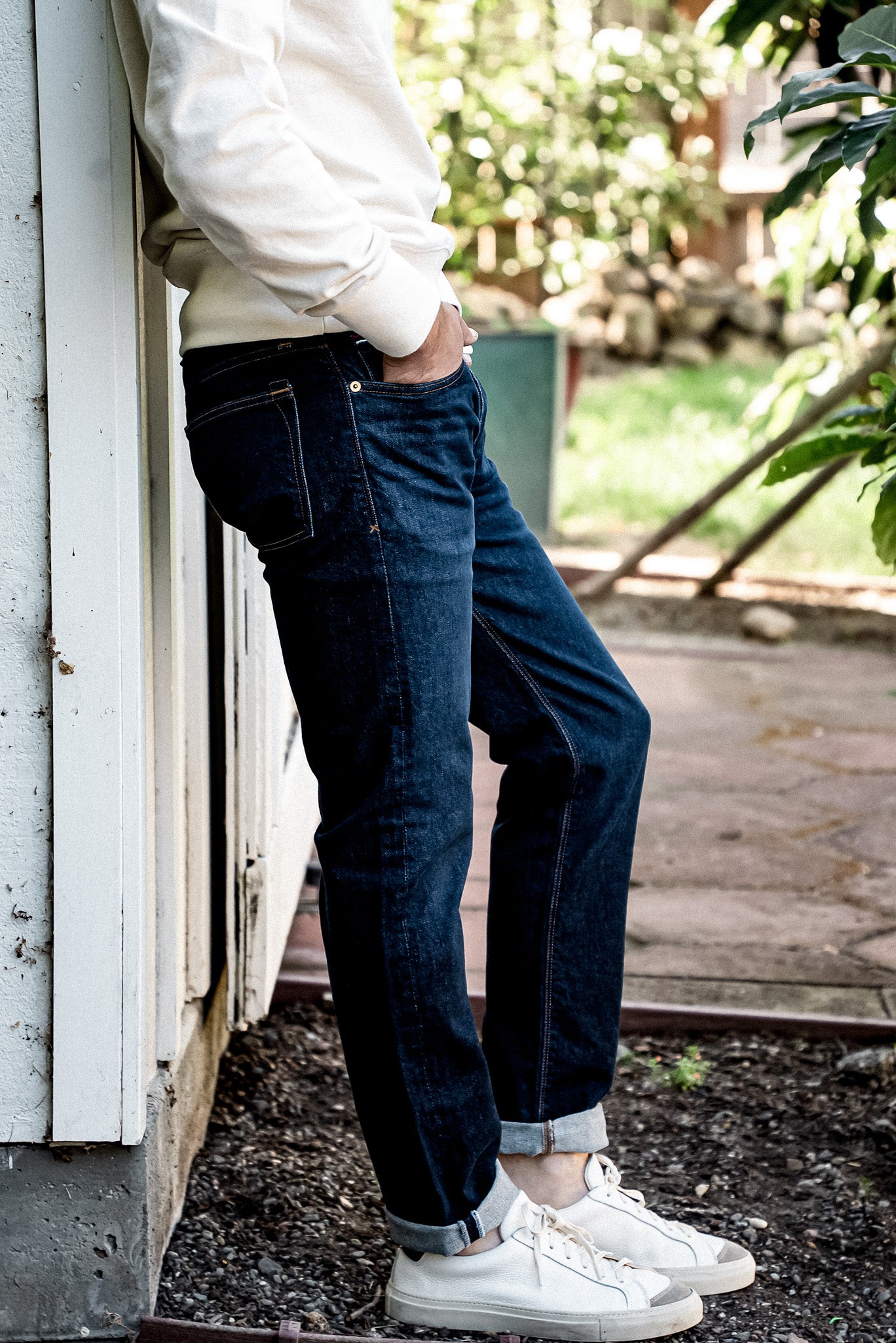 Side view of dark ocean wash straight slim fit jeans with cuffed hems, paired with a cream sweater and white sneakers.