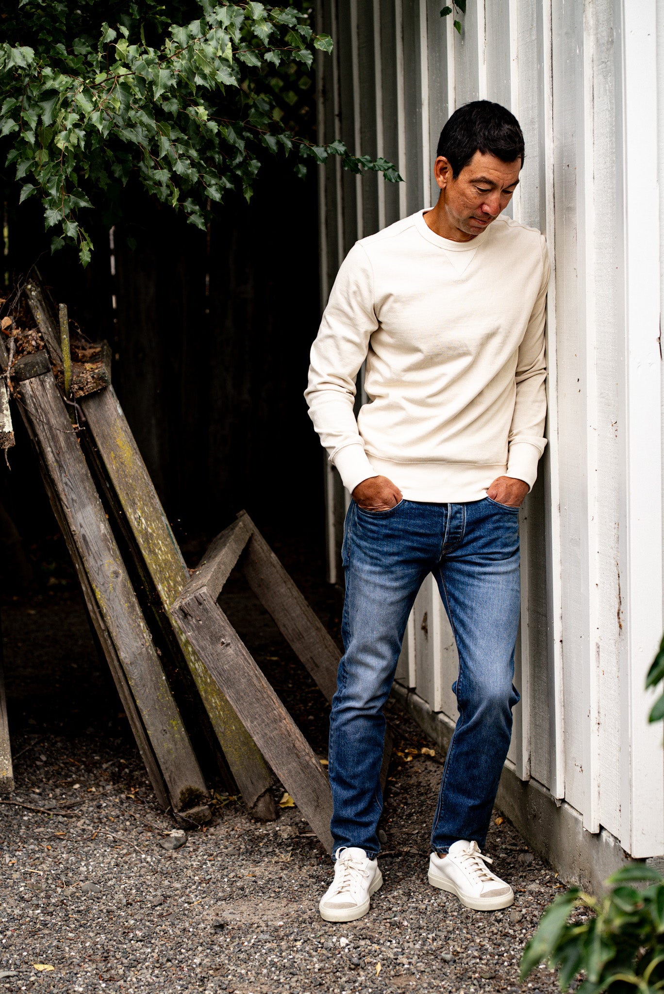 Man standing near a white wall wearing a white sweater and men's straight fit jeans made in USA