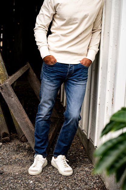 Man standing outdoors wearing men's straight slim fit jeans made in USA with a beige sweater