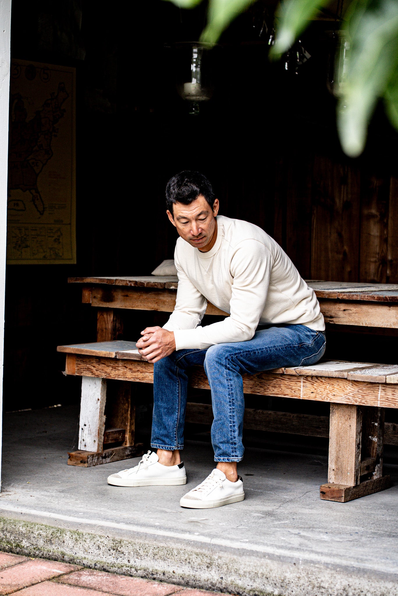 Man sitting on a wooden bench outdoors wearing slim fit jeans made in USA and a white sweater