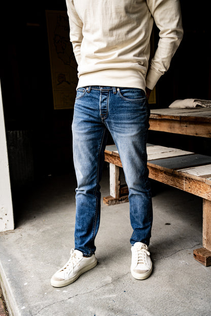 Man wearing men's premium denim jeans with a slim straight fit, cream sweater, and white sneakers