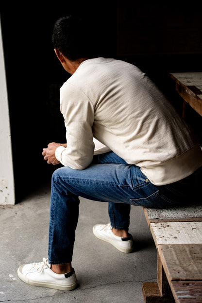 Man sitting on a wooden bench wearing men's slim fit denim jeans made in USA