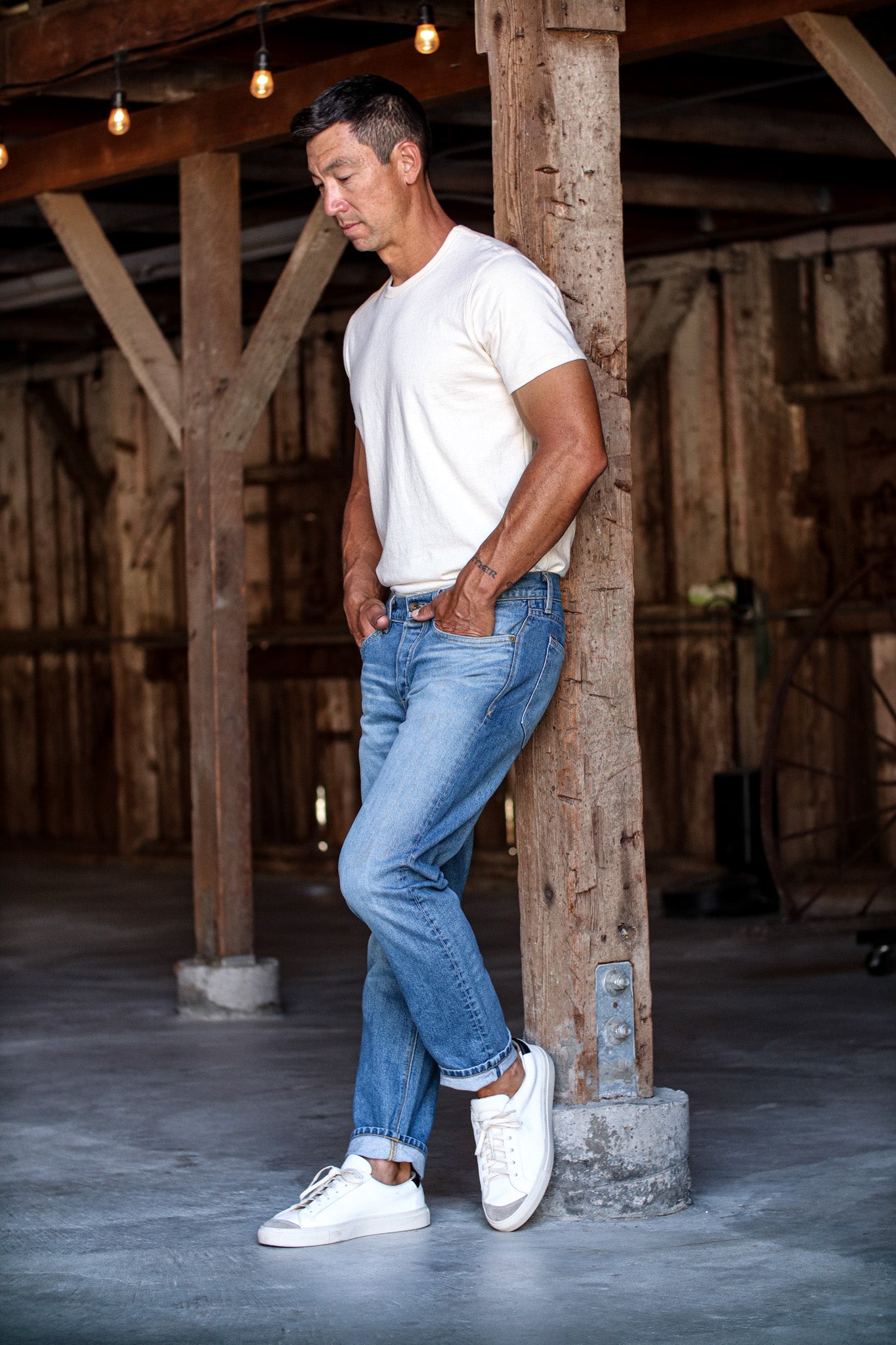 Men’s premium denim jeans shown on model, featuring a tailored fit with subtle fading and rolled cuffs, paired with a white tee and sneakers