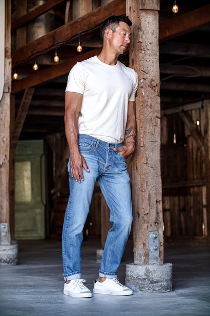 Men’s designer blue jeans shown on model, featuring a light washed finish, tapered fit, and rolled cuffs for a refined yet casual look paired with a simple white tee and sneakers