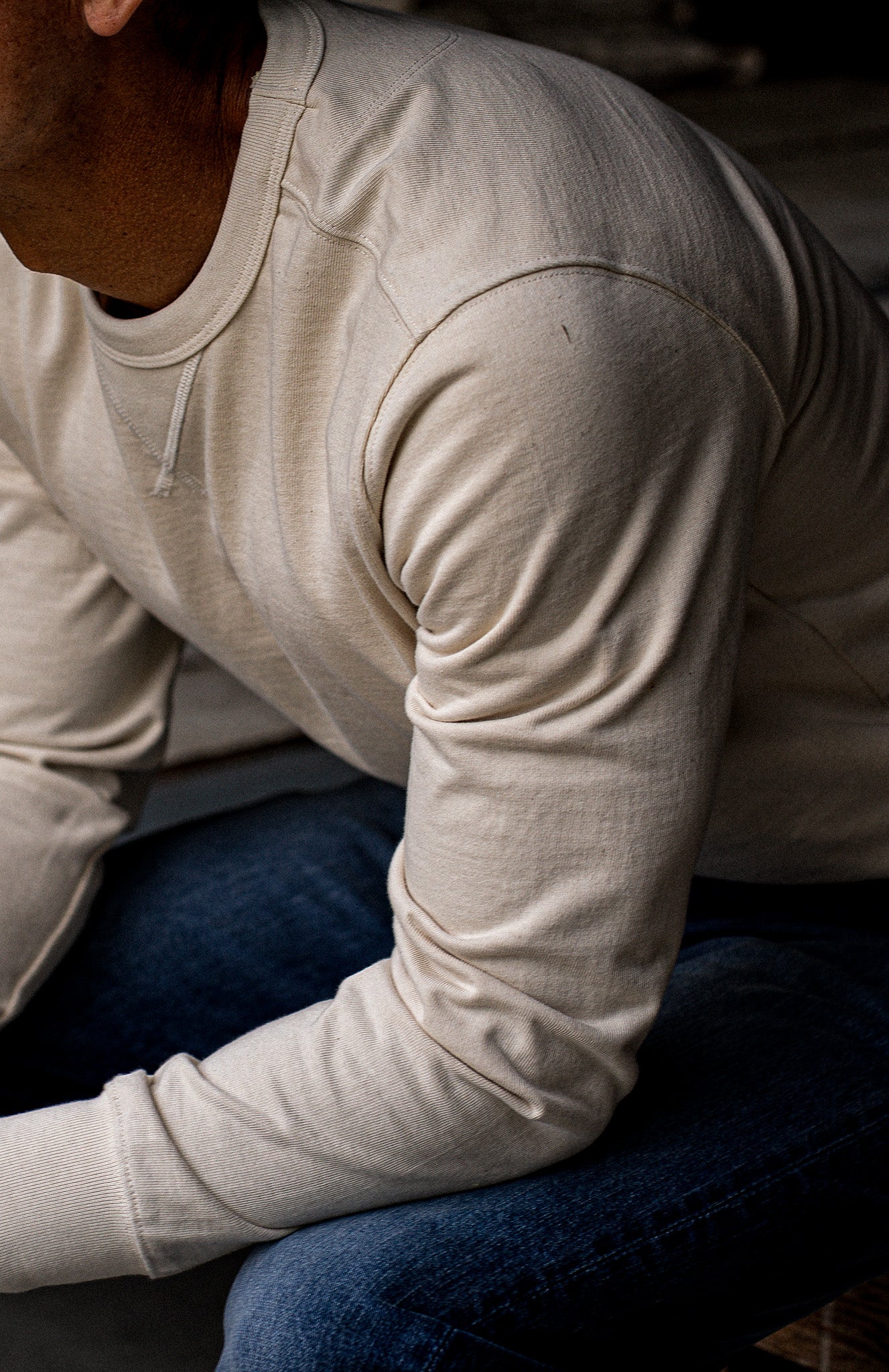 Close-up of the natural cotton Stinson rugby pullover showing crewneck stitching and shoulder seam, worn with blue denim.