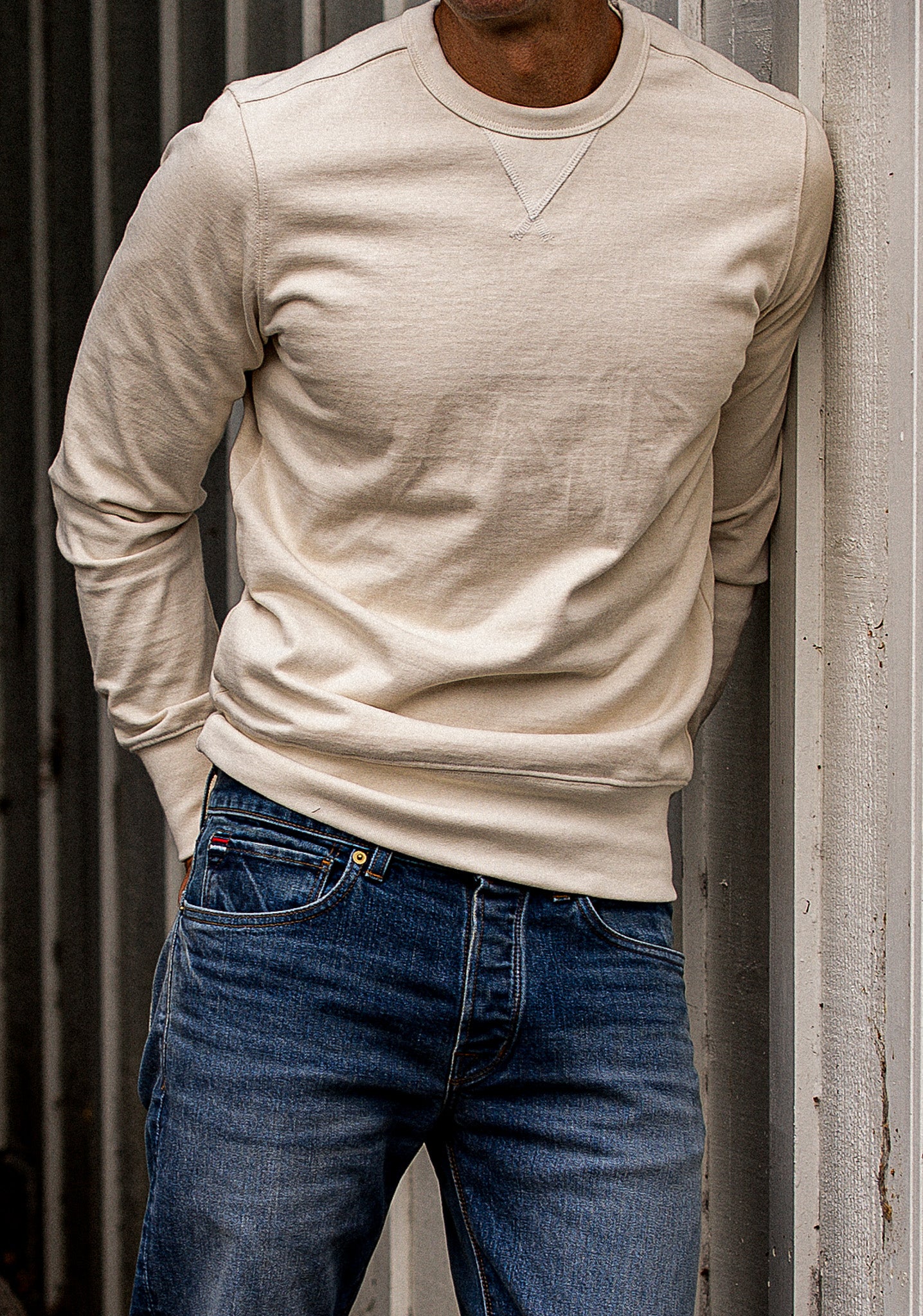 Natural Stinson pullover in heavyweight rugby jersey knit, worn with selvedge denim jeans against a metal wall.