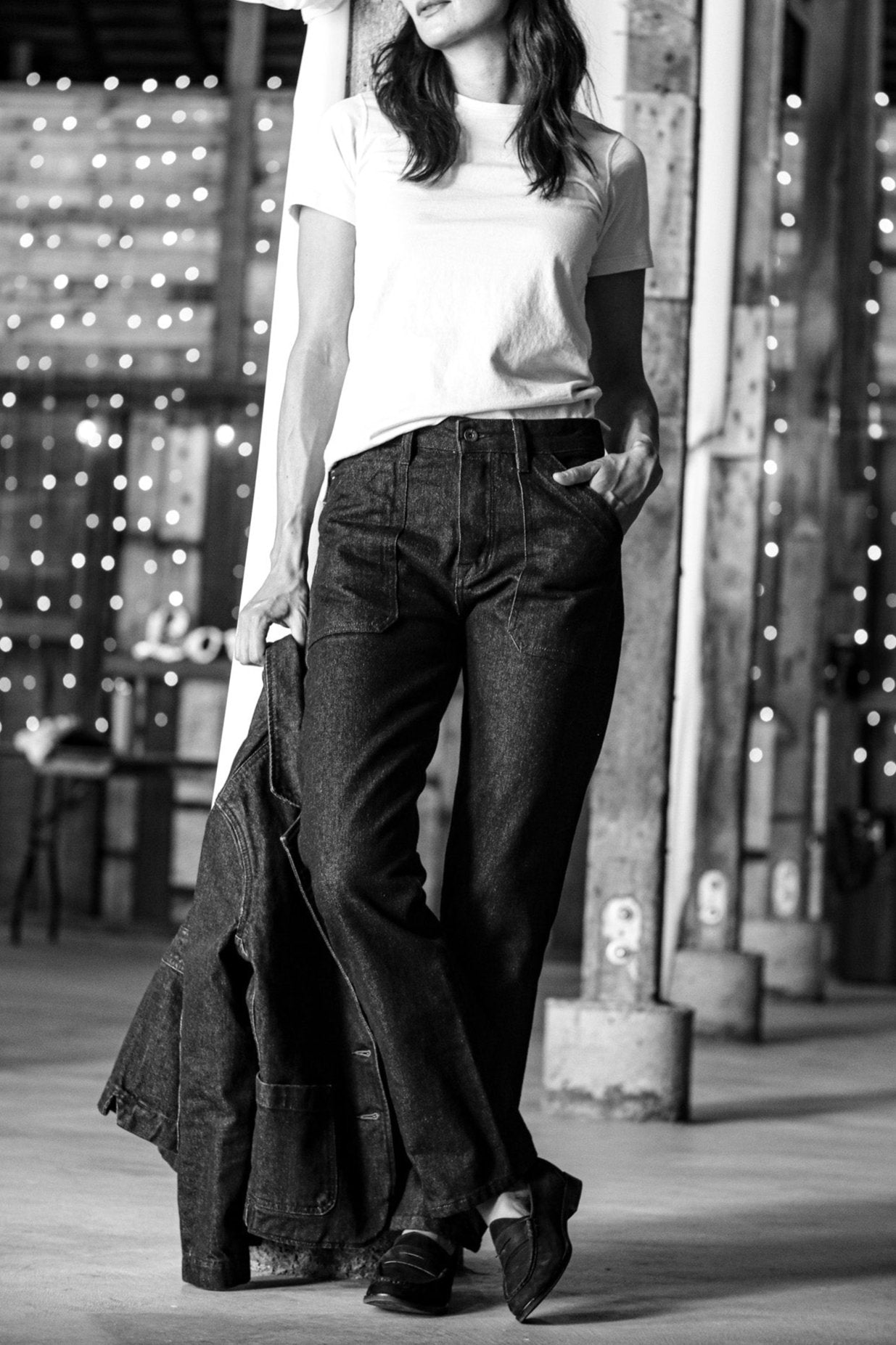 Woman styling the Reyes boxy tee in white with dark raw denim jeans and loafers in a warehouse setting.