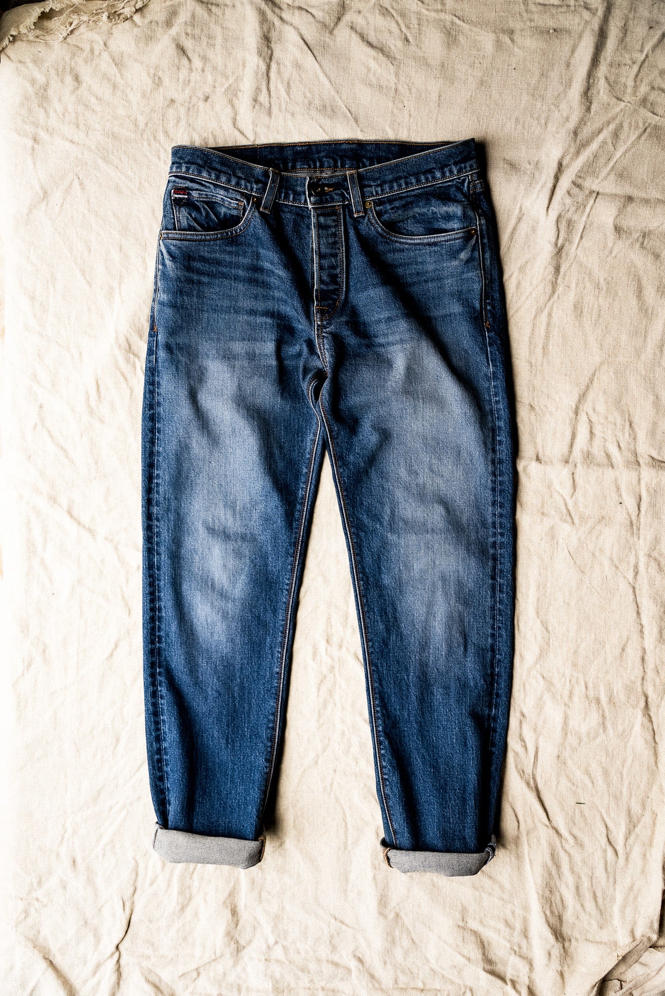 Pair of men's premium denim jeans laid flat on a textured beige surface