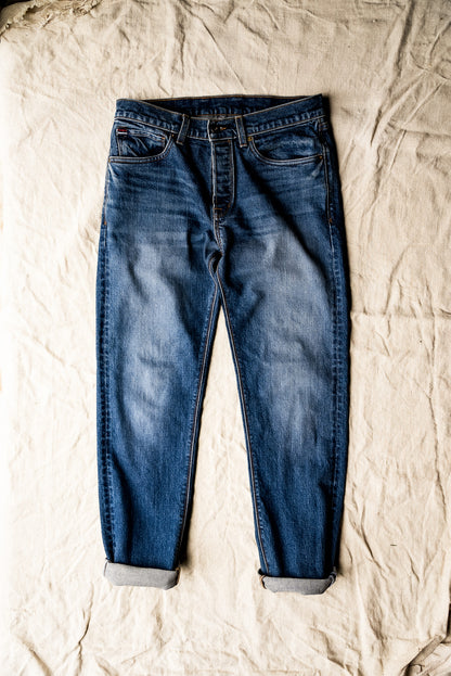Pair of men's premium denim jeans laid flat on a textured beige surface