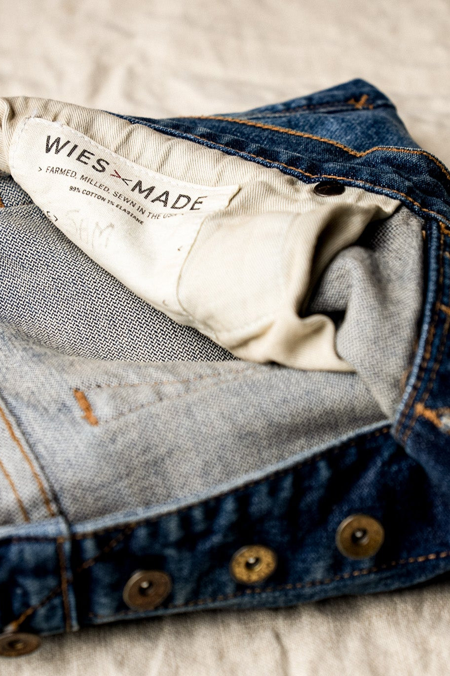 Men’s premium blue denim crafted from high-quality cotton with reinforced stitching, featuring a close-up of the branded inner label and durable hardware for a refined, authentic finish