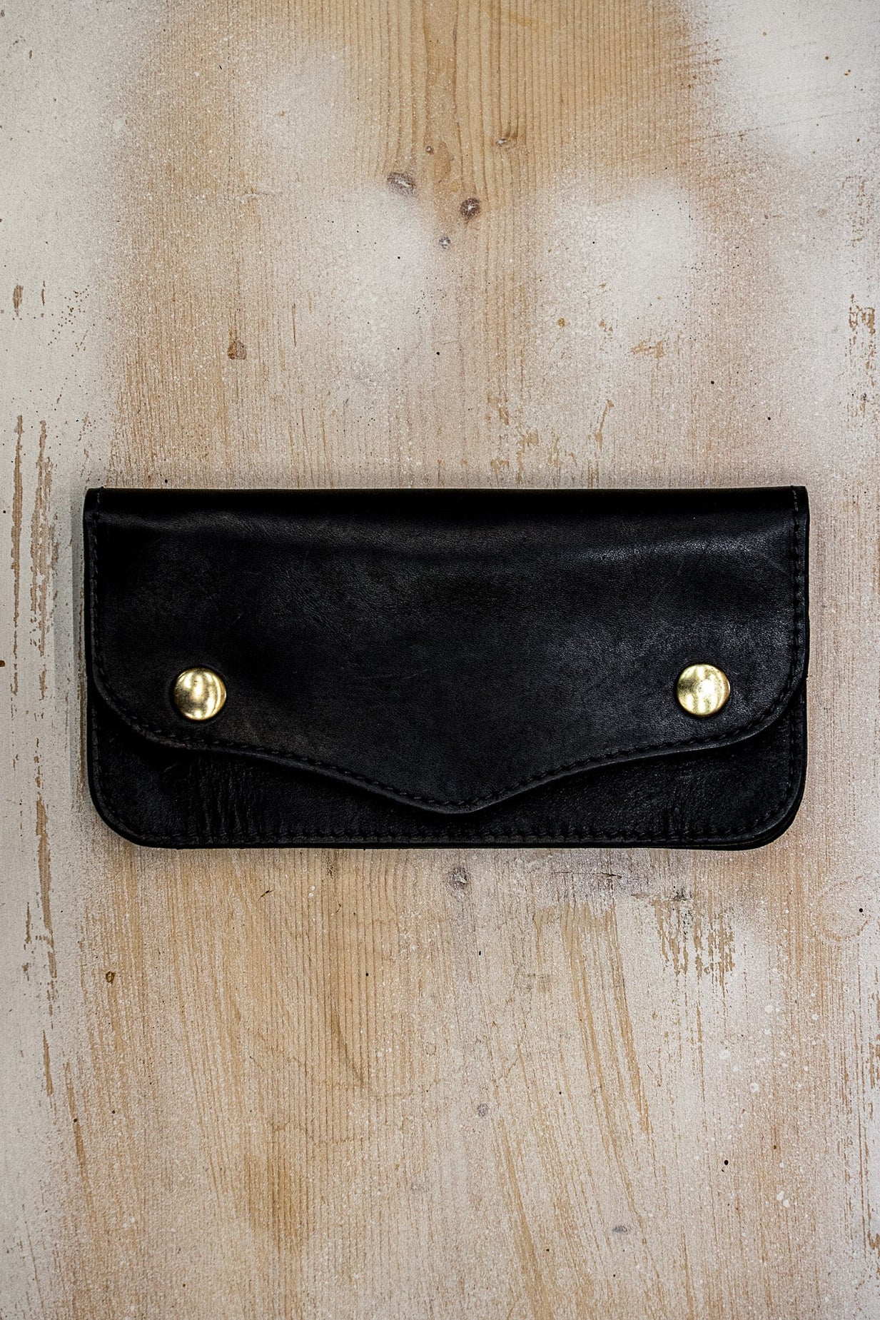 Black Horween leather Roper wallet with brass snap closures on a rustic wood surface.
