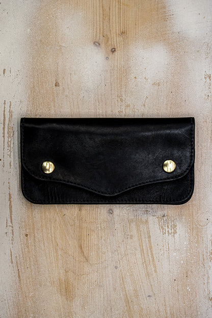 Black Horween leather Roper wallet with brass snap closures on a rustic wood surface.