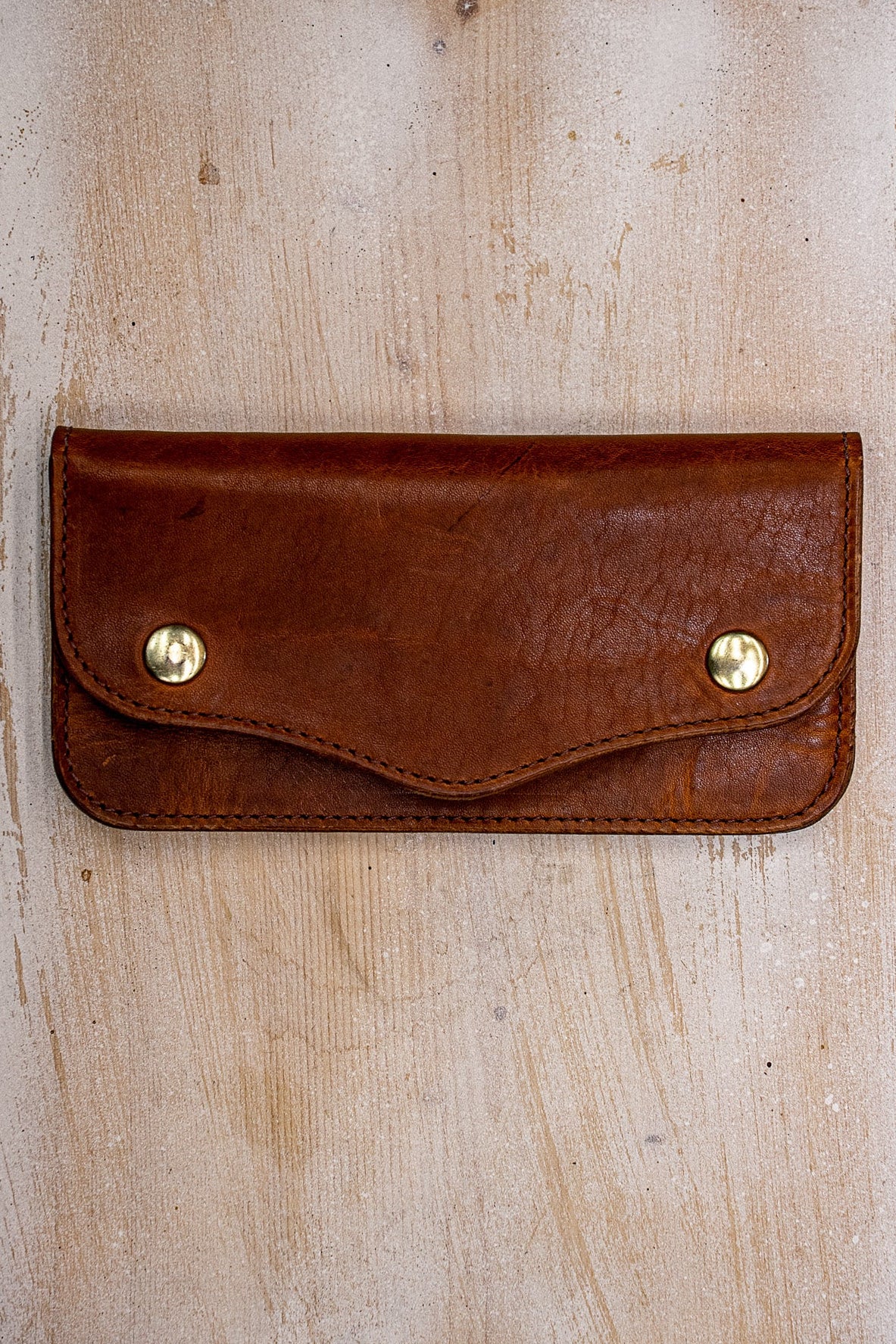 Tan Horween leather Roper wallet with brass snaps on weathered wood surface.