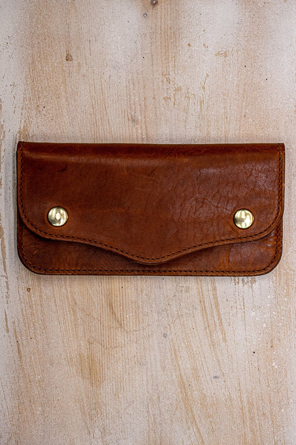 Tan Horween leather Roper wallet with brass snaps on weathered wood surface.