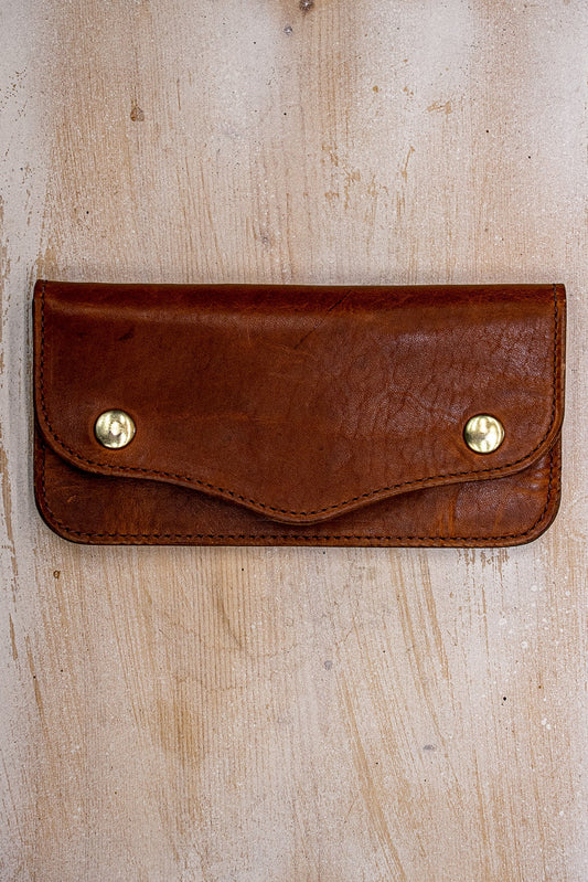 Tan Horween leather Roper wallet with brass snaps on weathered wood surface.