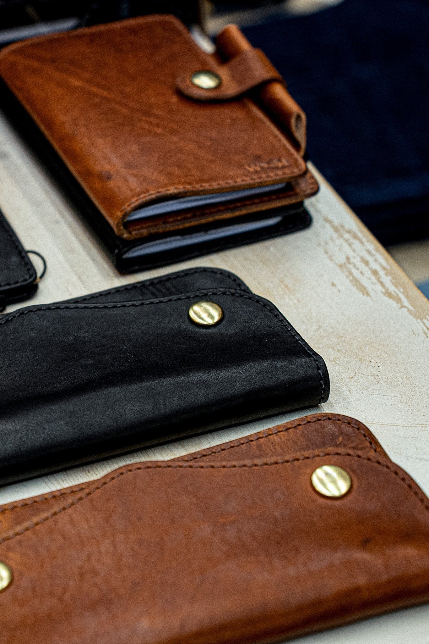 Tan and black Roper wallets in Horween leather with brass snap closures on a bench.