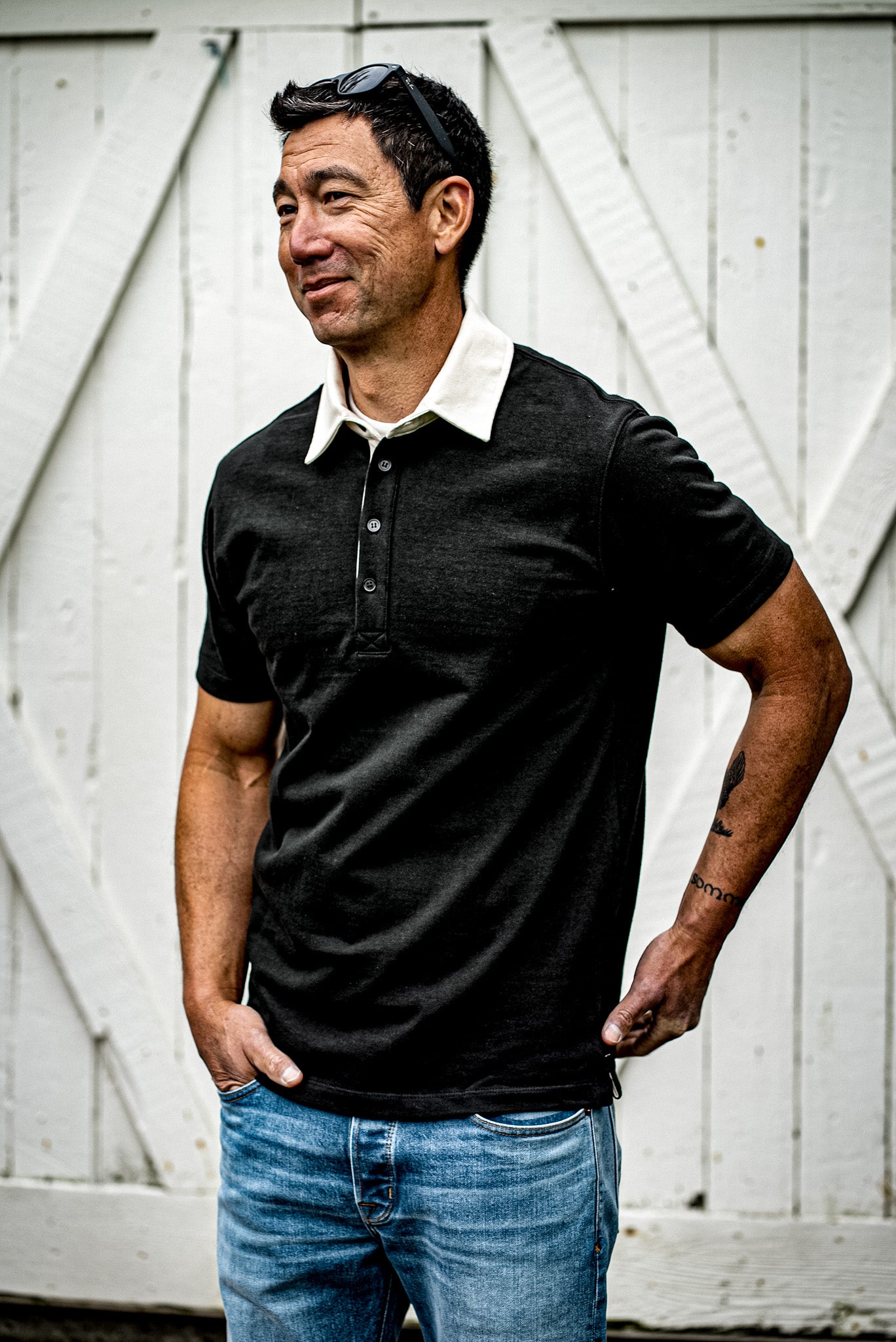 Man wearing black rugby polo shirt with white collar and blue jeans outdoors