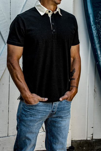 Men's black rugby polo shirt with cream contrast collar, paired with jeans