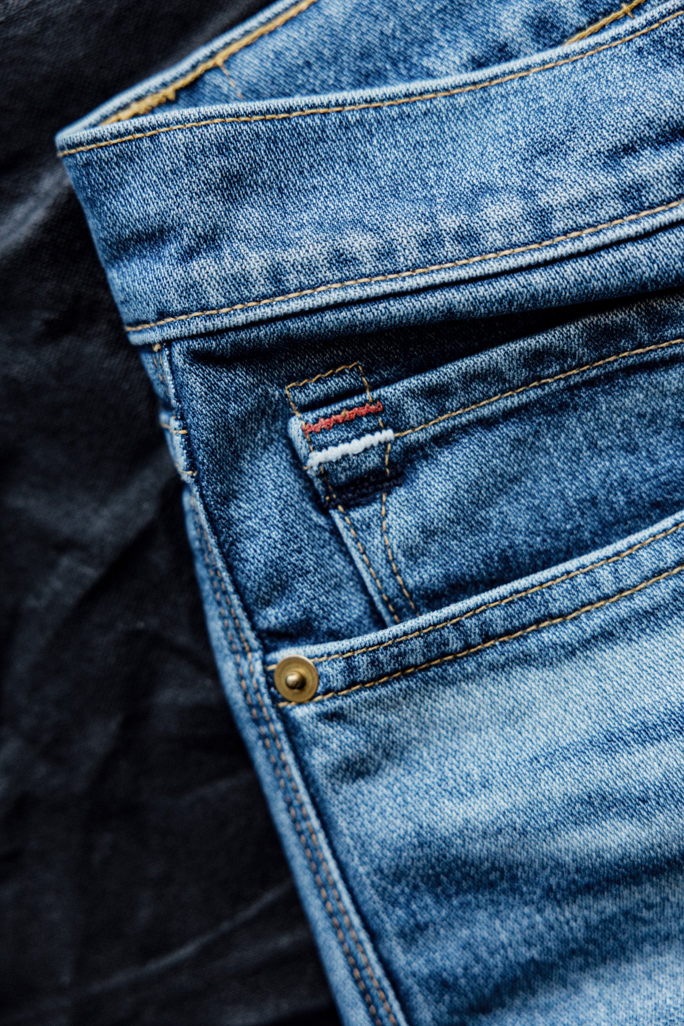 Close-up of salt-wash denim jean pocket with brass rivet and contrast stitching.