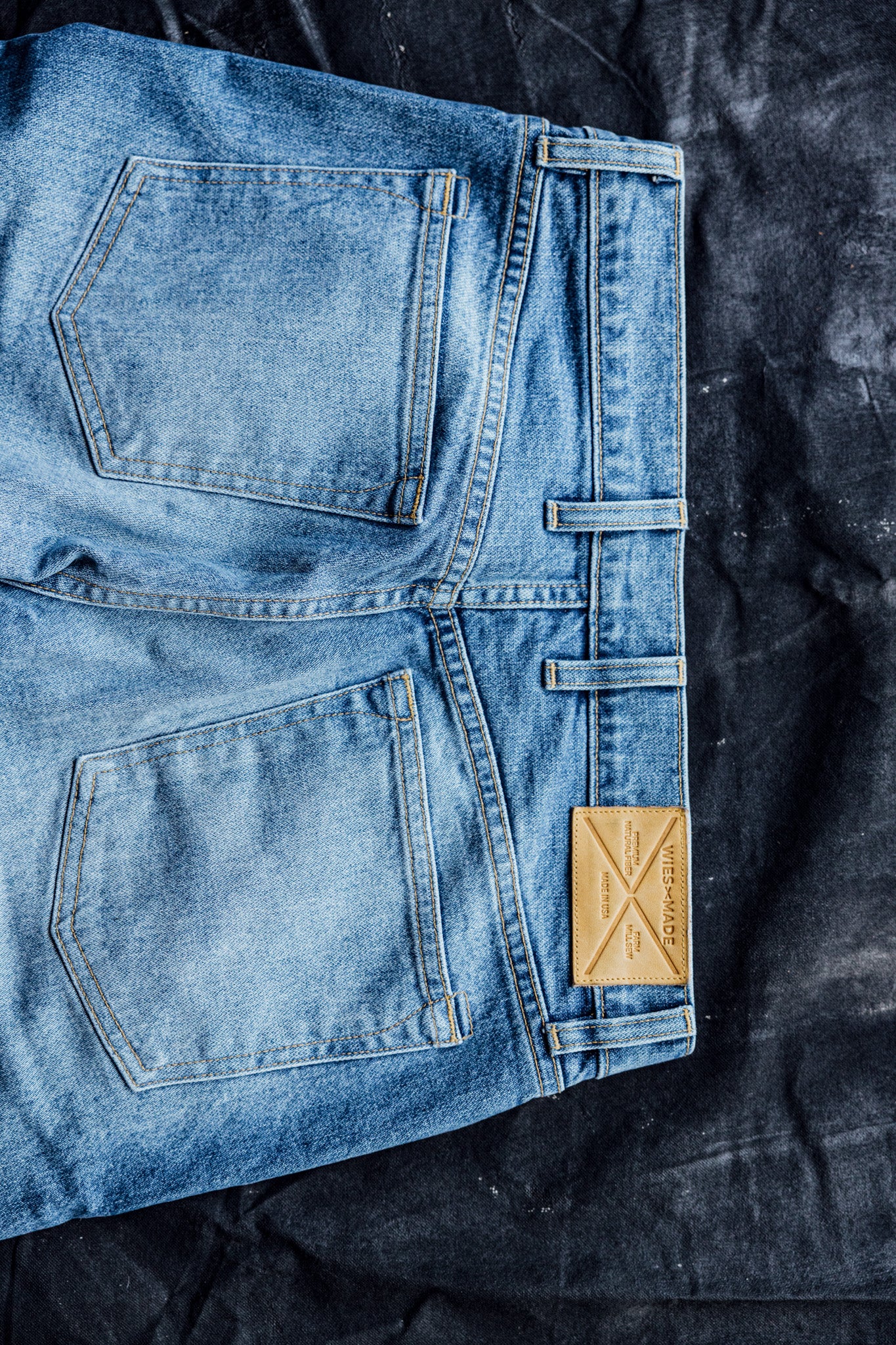 Folded salt wash American made denim jeans showing back pockets and leather WiesMade patch.