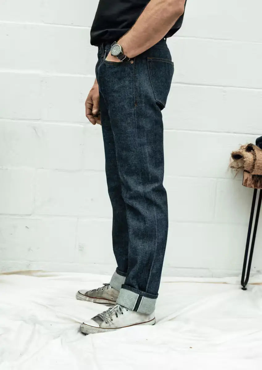 Man wearing a Sam Fit jeans in Raw Selvedge color featuring a clean, straight-leg fit and rolled cuffs highlighting the selvedge edge