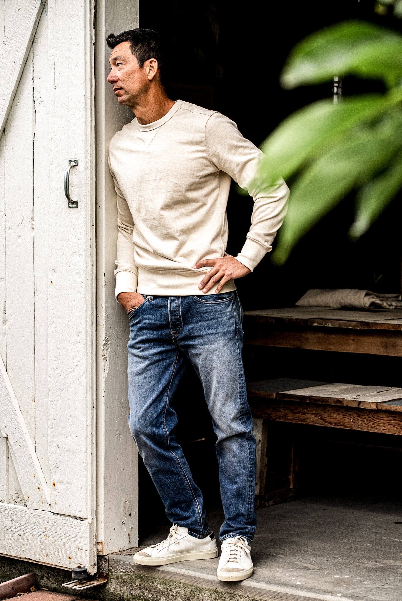 Men’s premium denim jeans styled with a cream crewneck and sneakers, featuring a straight leg fit, medium blue wash, and subtle fading for a relaxed yet refined look
