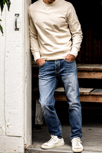 American made men’s denim jeans styled with a cream sweatshirt and white sneakers, featuring a straight leg fit, light fading, and durable stitching for a refined casual look