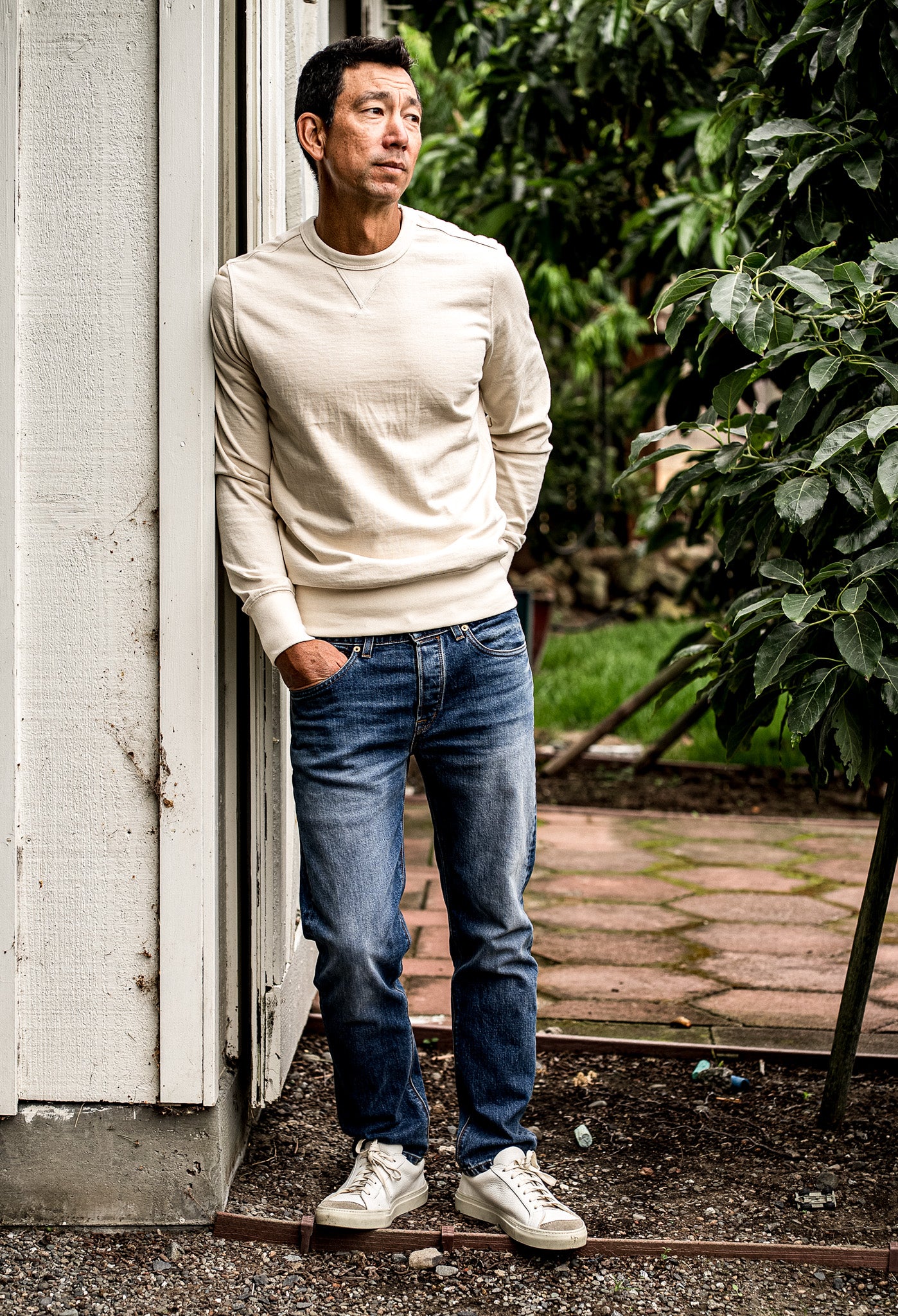 Premium blue denim jeans for men paired with a cream sweatshirt and white sneakers, featuring a modern straight leg cut, medium wash, and subtle whiskering for a refined casual look