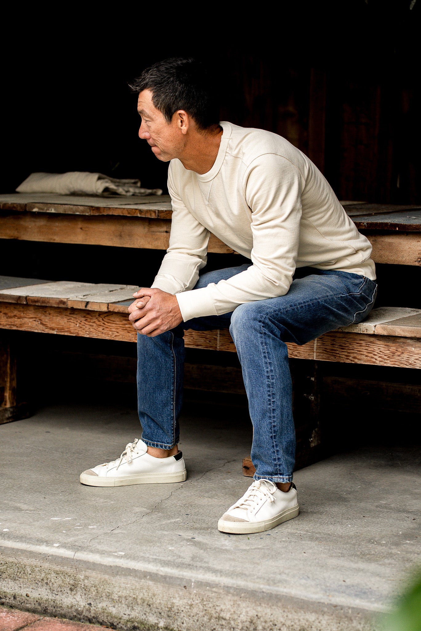 Men’s premium blue jeans paired with a cream sweatshirt and white sneakers, designed with a slim straight fit, medium wash tone, and soft fade for a comfortable yet elevated everyday look