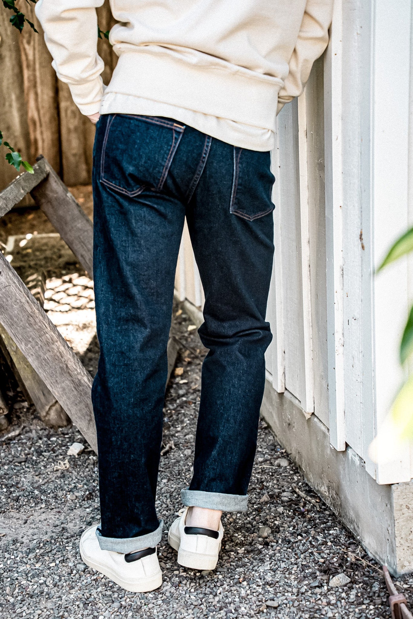 Back view of dark ocean wash American made denim jeans with cuffed hems, paired with cream sweatshirt and white sneakers.