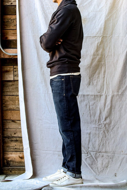 Side profile of model wearing dark ocean wash standard fit jeans with cuffed selvedge hem, black hoodie, and white sneakers.
