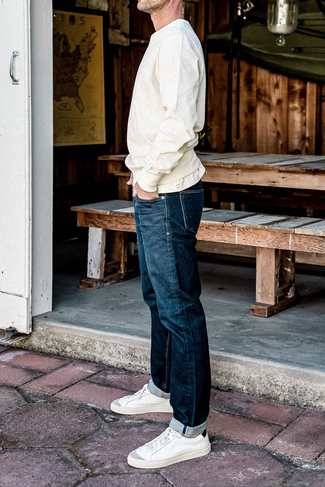 Side view of dark ocean wash American made denim jeans with cuffed hem, paired with cream sweatshirt and white sneakers.